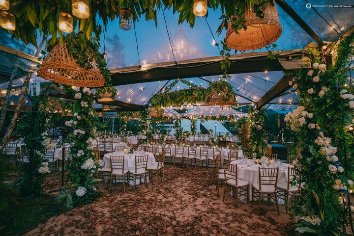 Glass marquee dinner set with hanging rattan lamps and floral arches